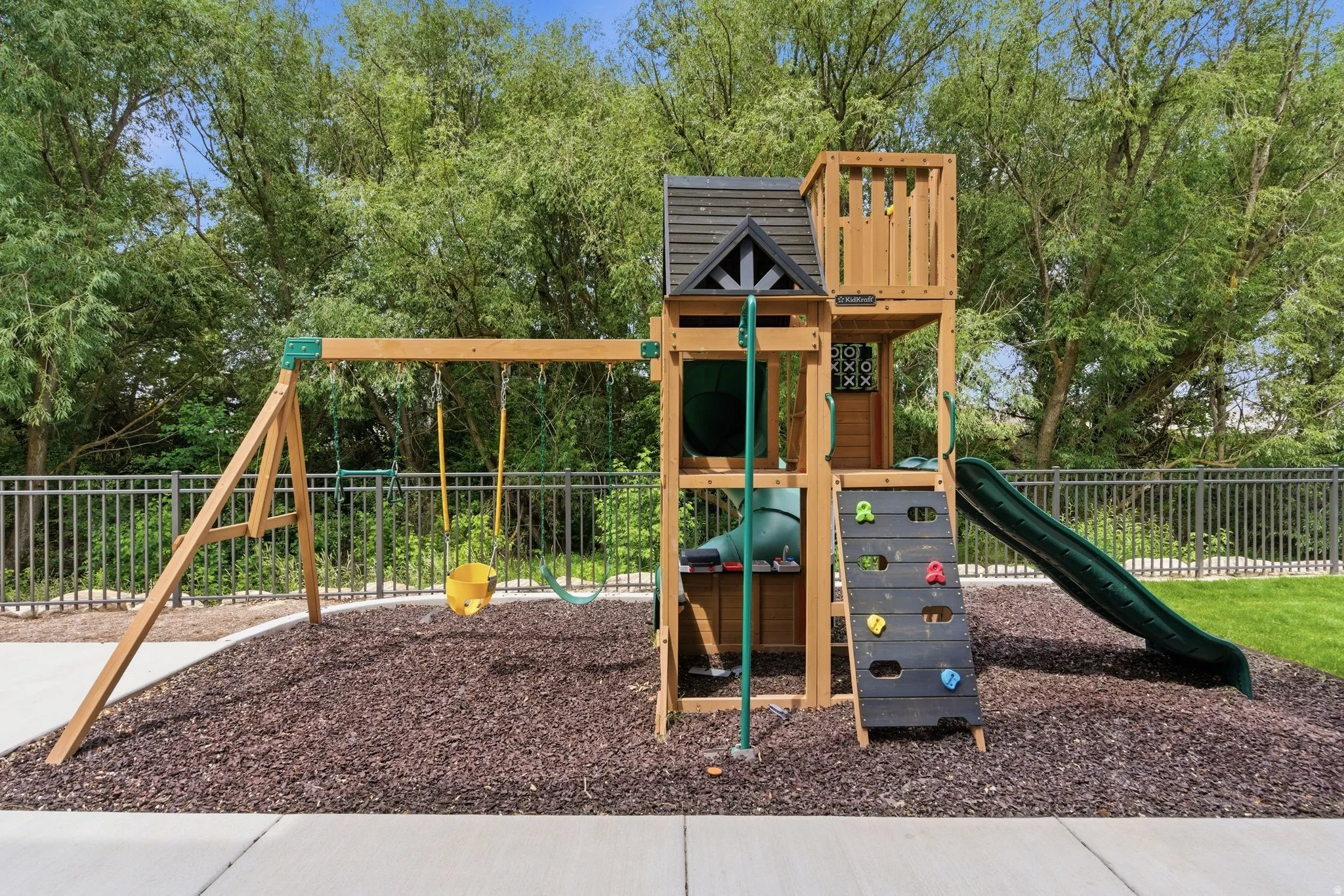 Outdoor play structure featuring a wooden swing set, slide, and rock-climbing wall