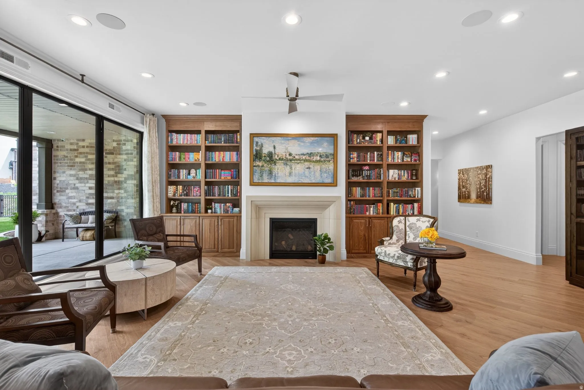 Living area featuring gas fireplace with a stone surround, integrated wood built-in bookcases, wood-finish flooring, and recessed lighting