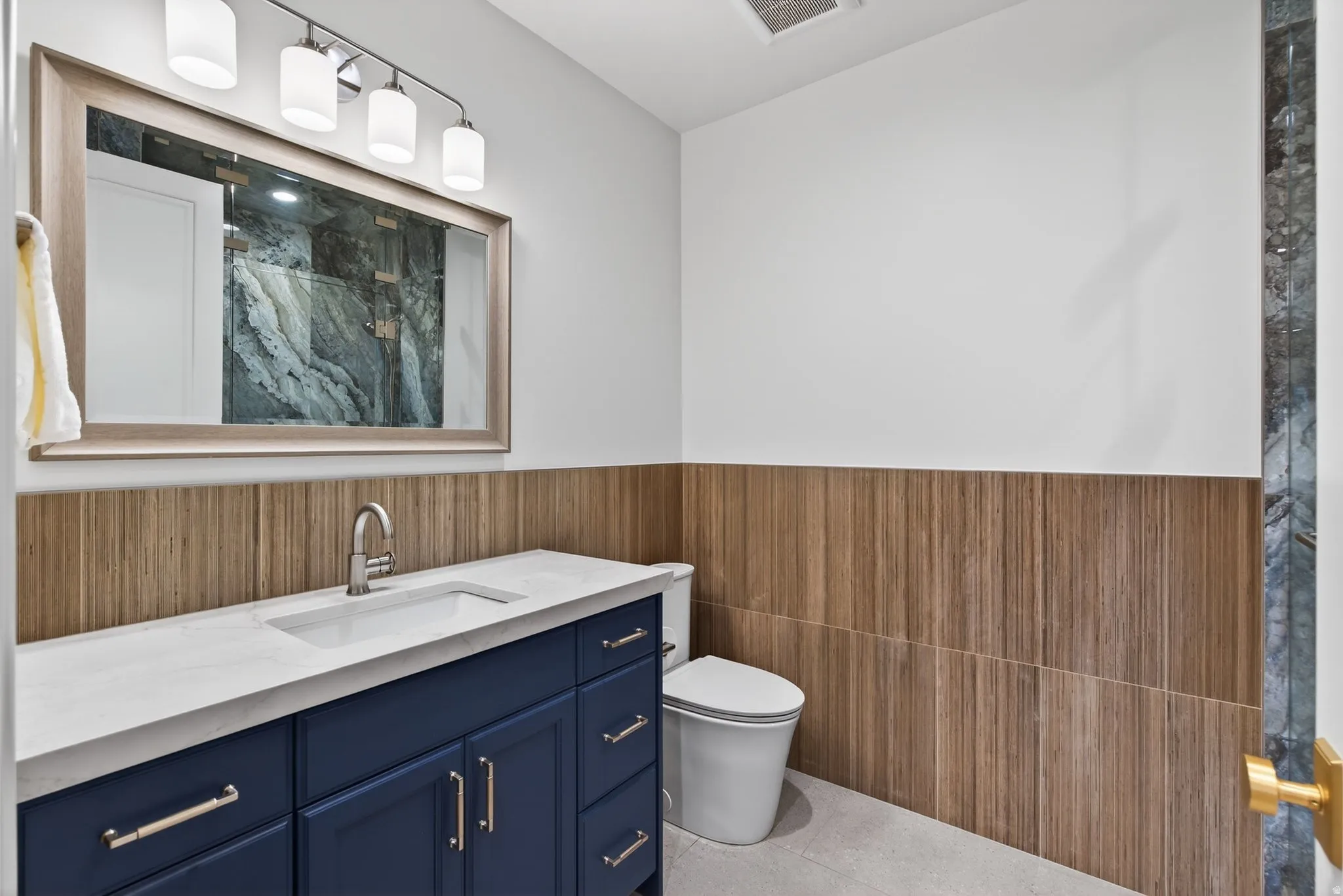 Lower Level Full bathroom with vanity, a wainscoted wall, tile walls, a marble finish shower, and light tile patterned floors