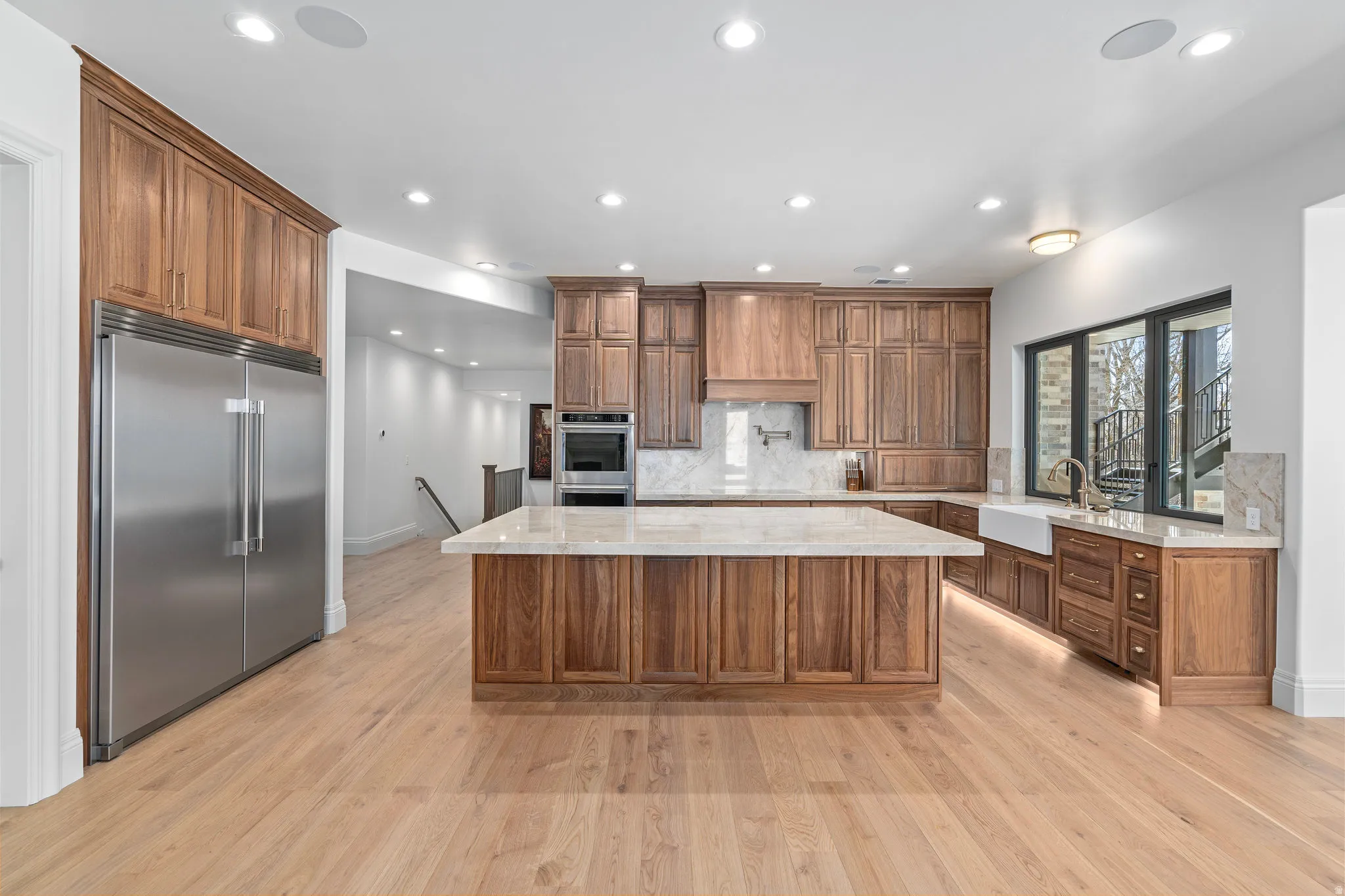 Lower Level Quartzite backsplash, walnut cabinetry, double ovens, pot filler, beautiful walnut stove hood