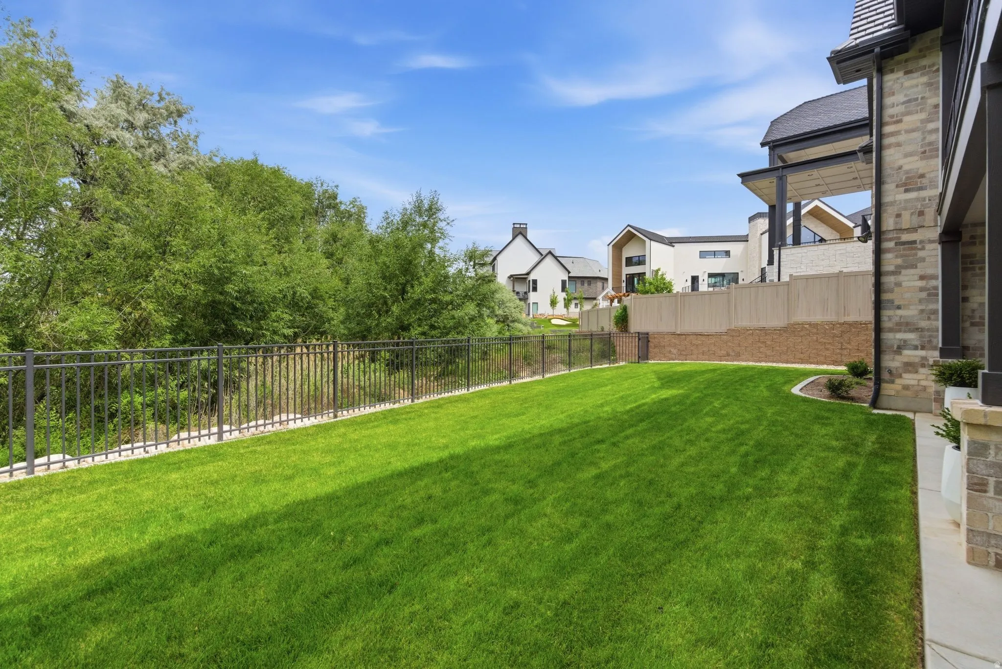 Expansive green lawn bordered by a metal fence, mature trees, and a stone retaining wall