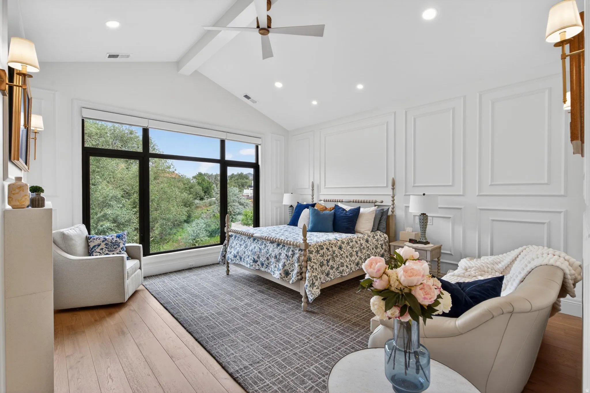 Expansive window wall with black framing, vaulted ceiling with exposed beam, recessed lighting, wood-finish flooring, and decorative wall molding