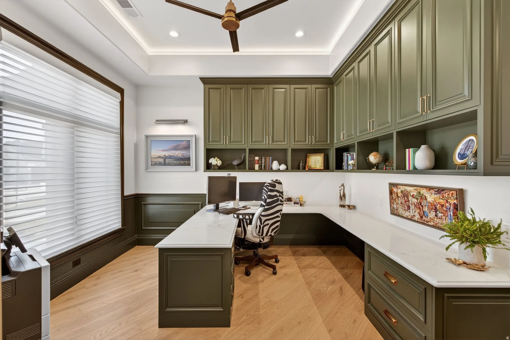 Office space with built in desk, wainscoting, light wood finished floors, a ceiling fan, and recessed lighting, quartz counter top