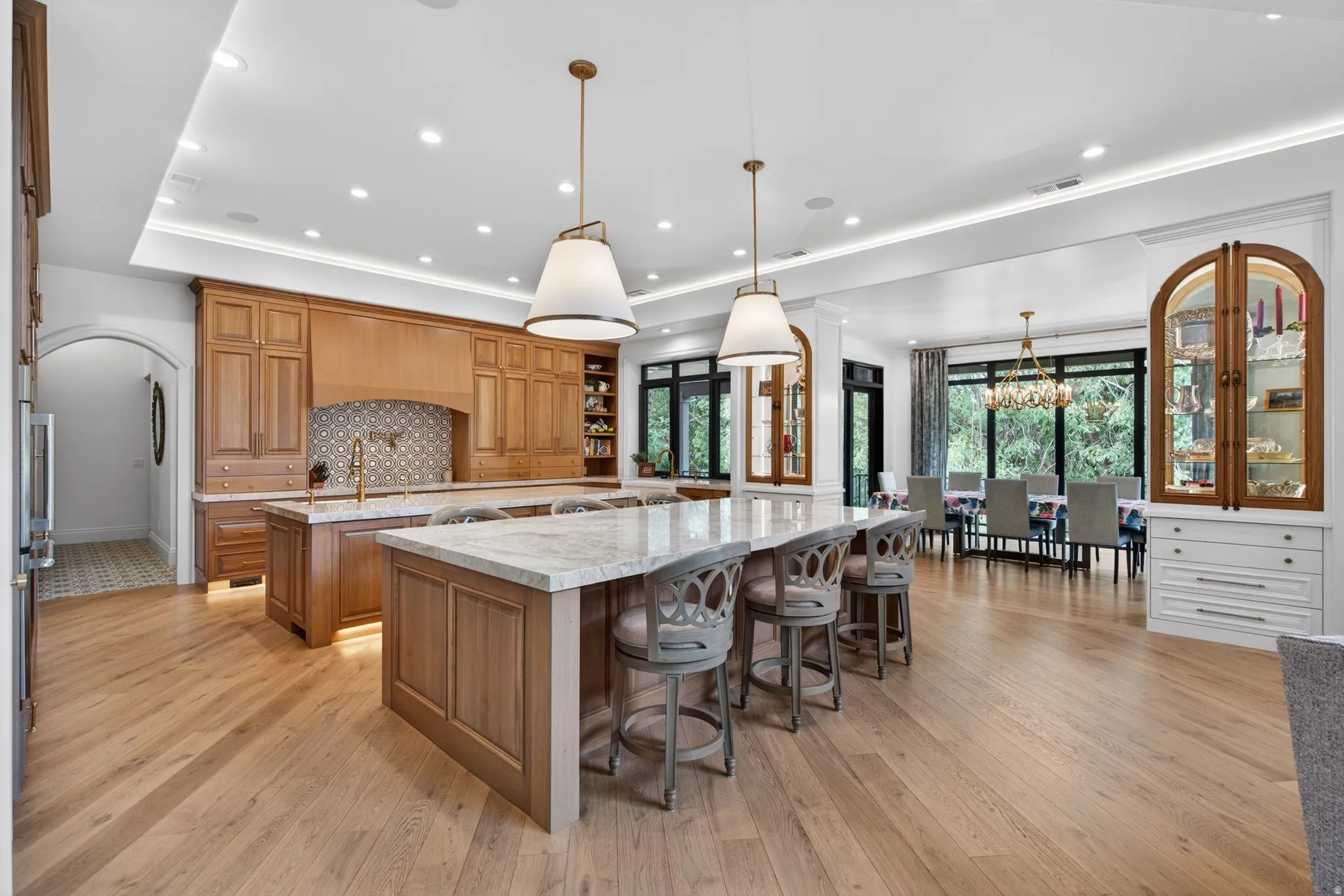 Expansive kitchen featuring wood-finish flooring, custom wood cabinetry, a decorative tile backsplash, and 2 large islands