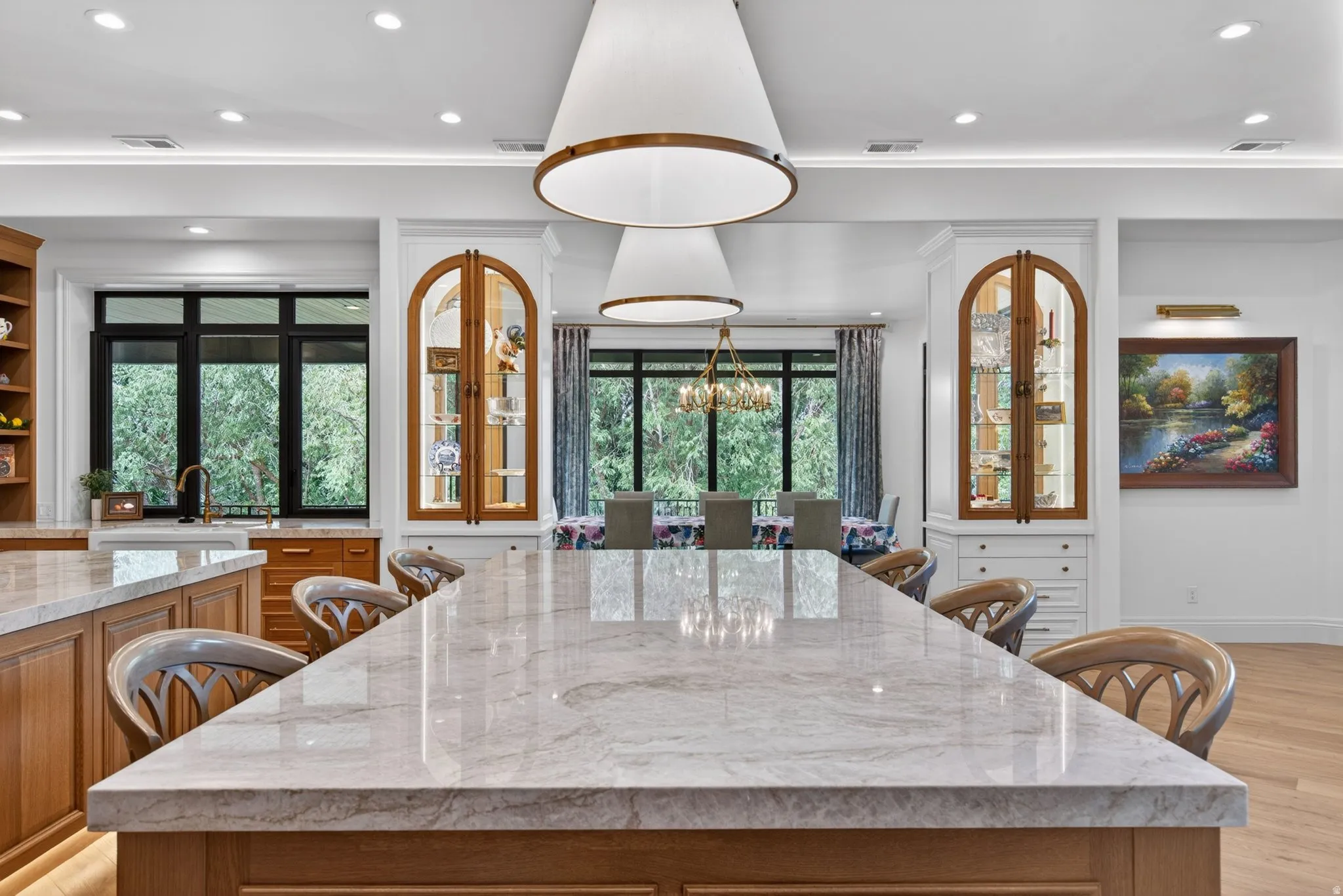 Expansive kitchen island with a quartzite countertop, recessed lighting, architectural pendant lights, integrated cabinetry, and arched display cabinets