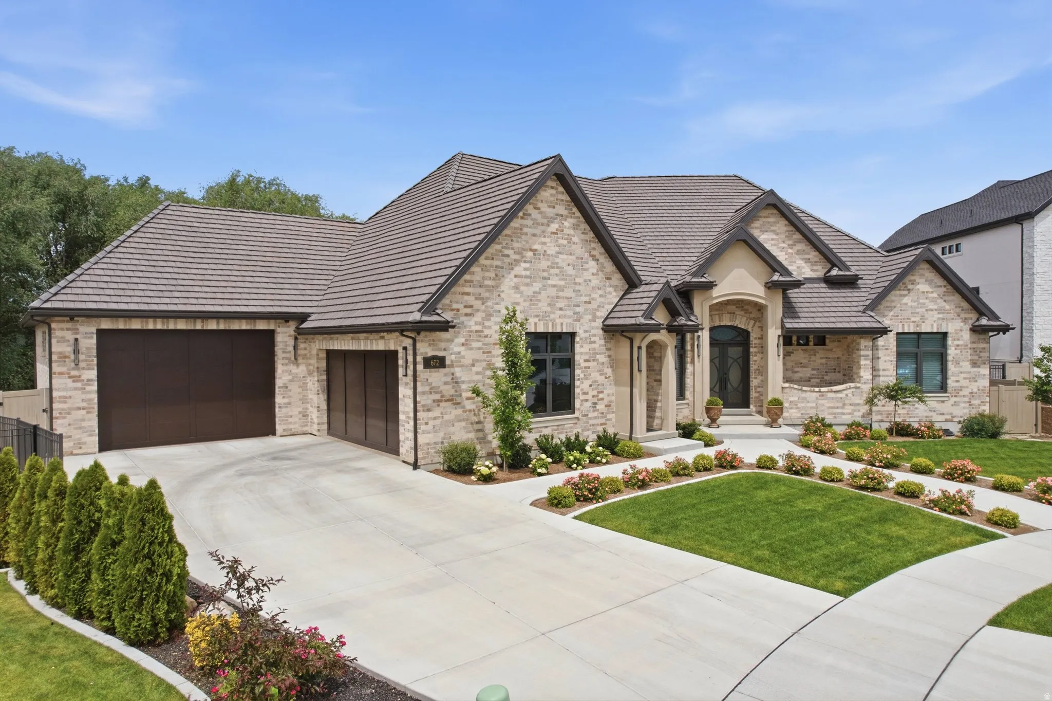 Stone facade residence featuring a tiled roof, multi-car garage, manicured landscaping, and a grand arched entryway