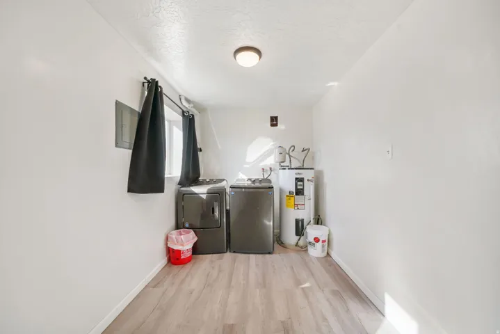 Laundry area featuring washing machine and dryer, light wood finished floors, electric water heater, a textured ceiling, and electric panel