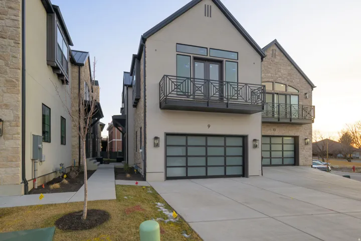 View of front of home featuring a garage, stucco siding, stone siding, a balcony, and driveway