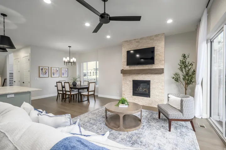 Living area with wood finished floors, a stone fireplace, ceiling fan, and a chandelier