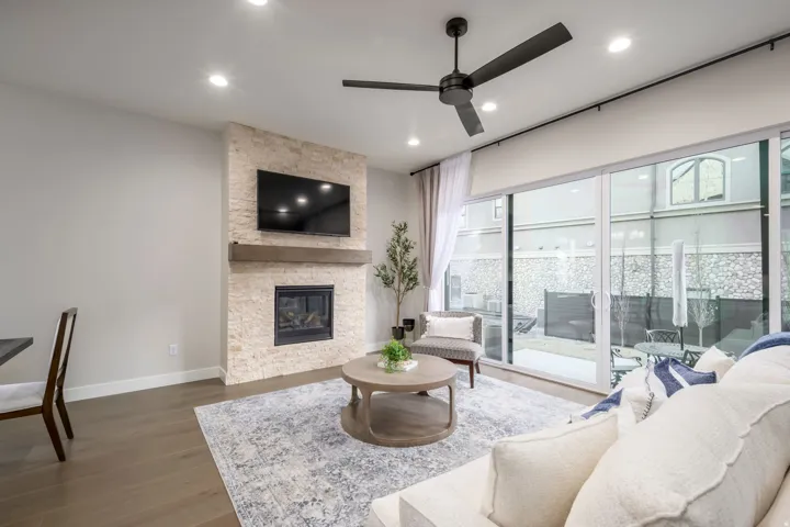Living area featuring a stone fireplace, a ceiling fan, wood finished floors, and recessed lighting