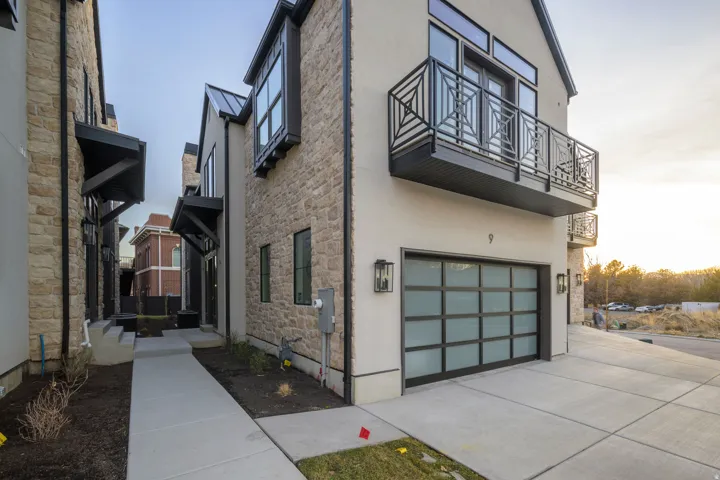 Property exterior at dusk with a balcony, a garage, stone siding, stucco siding, and concrete driveway
