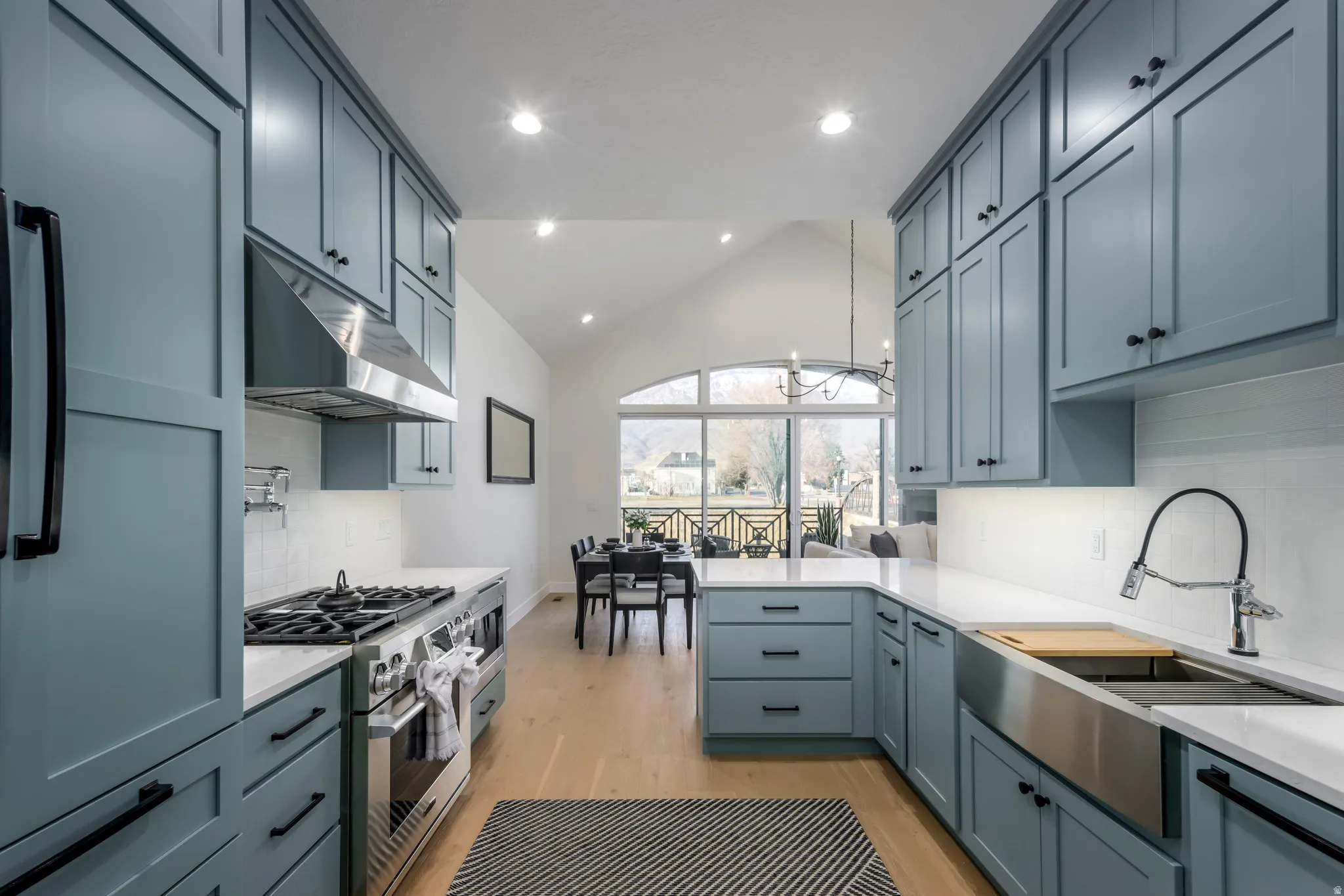 Kitchen with lofted ceiling, high end stainless steel range, light wood finished floors, tasteful backsplash, and light stone counters