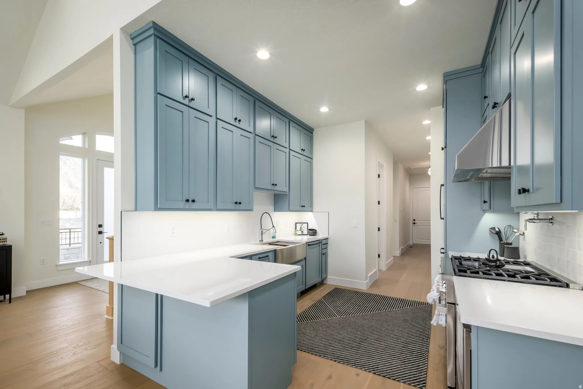 Kitchen featuring blue cabinets, gas stove, a peninsula, light stone counters, and light wood-type flooring