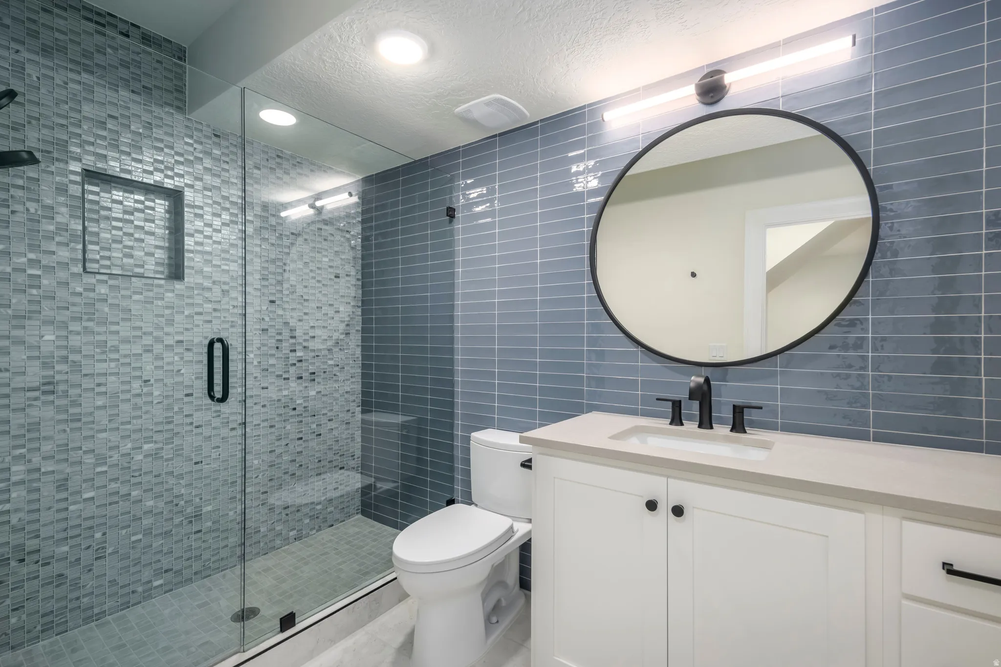 Full bathroom featuring tile walls, vanity, a shower stall, a textured ceiling, and decorative backsplash