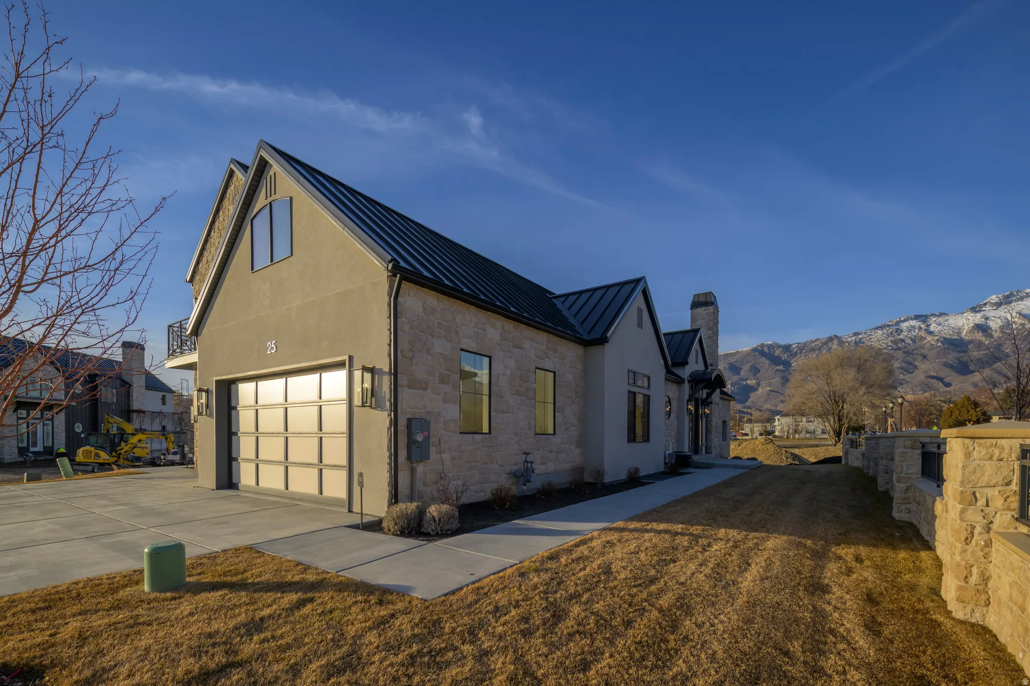 View of side of home featuring a standing seam roof, stone siding, driveway, stucco siding, and a mountain view