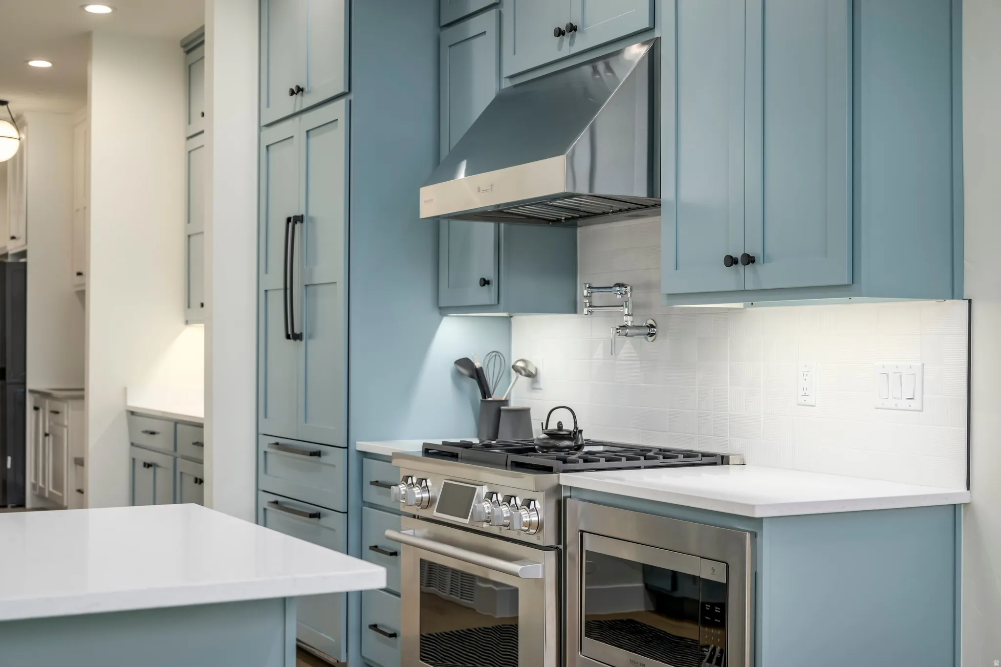 Kitchen with stainless steel appliances, blue cabinetry, decorative backsplash, and light stone countertops
