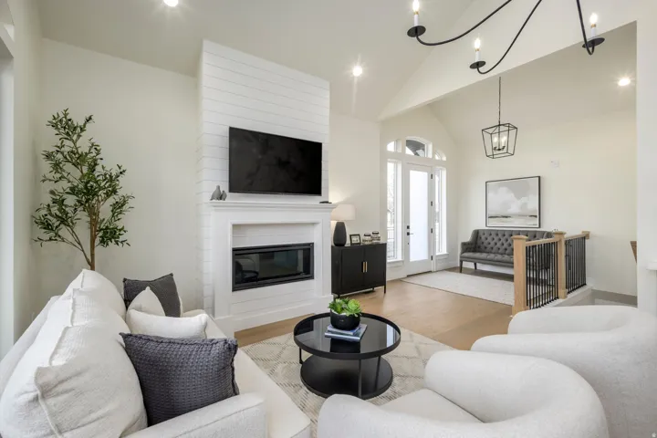 Living room with wood finished floors, vaulted ceiling, a large fireplace, and a chandelier