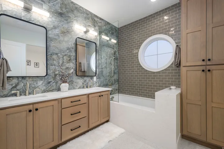 Full bath featuring double vanity, tile walls, and a combined bath / shower with marble appearance
