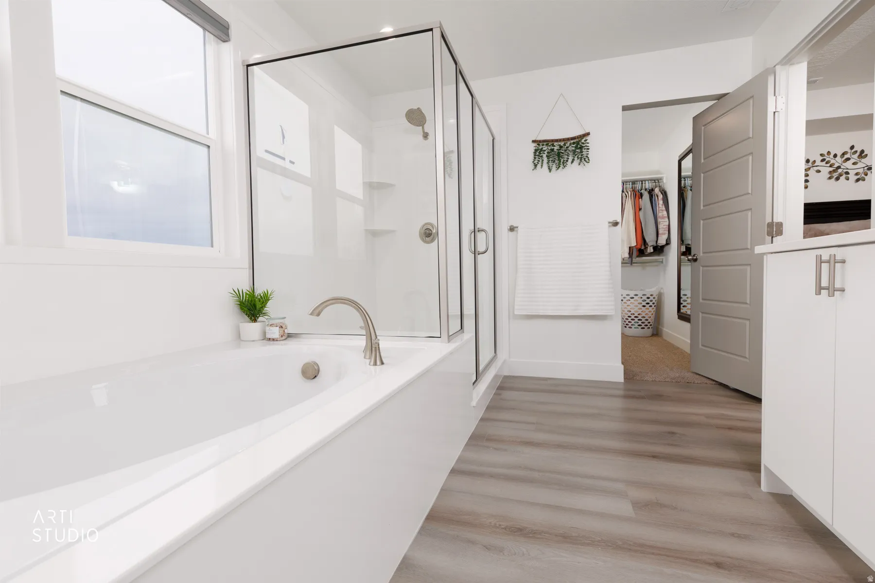 Bathroom featuring a stall shower, a walk in closet, light wood finished floors, and a bath