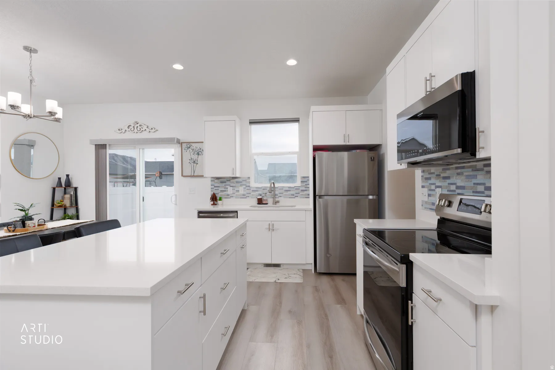 Kitchen with stainless steel appliances, light wood-style flooring, white cabinetry, suspended lighting, and a center island
