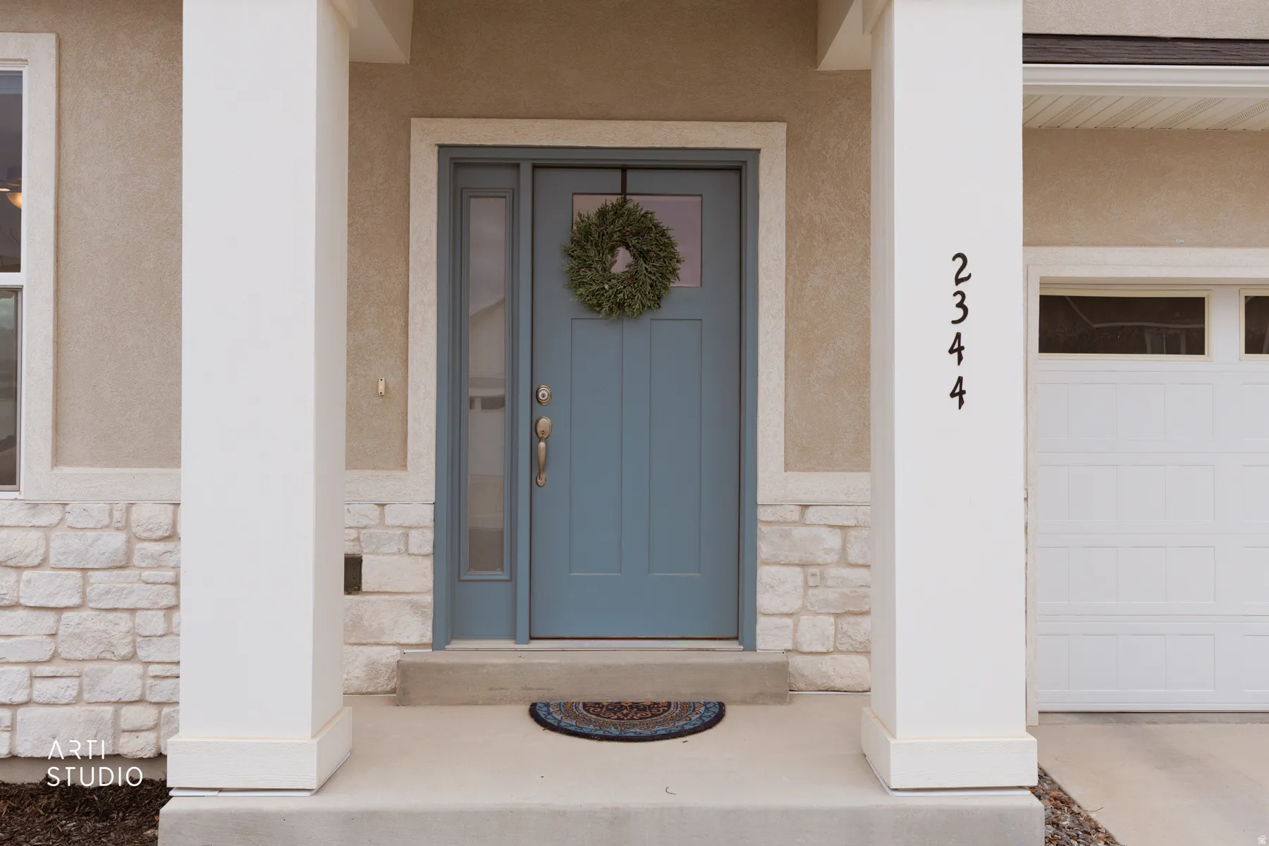 View of exterior entry with stone siding, a garage, and stucco siding