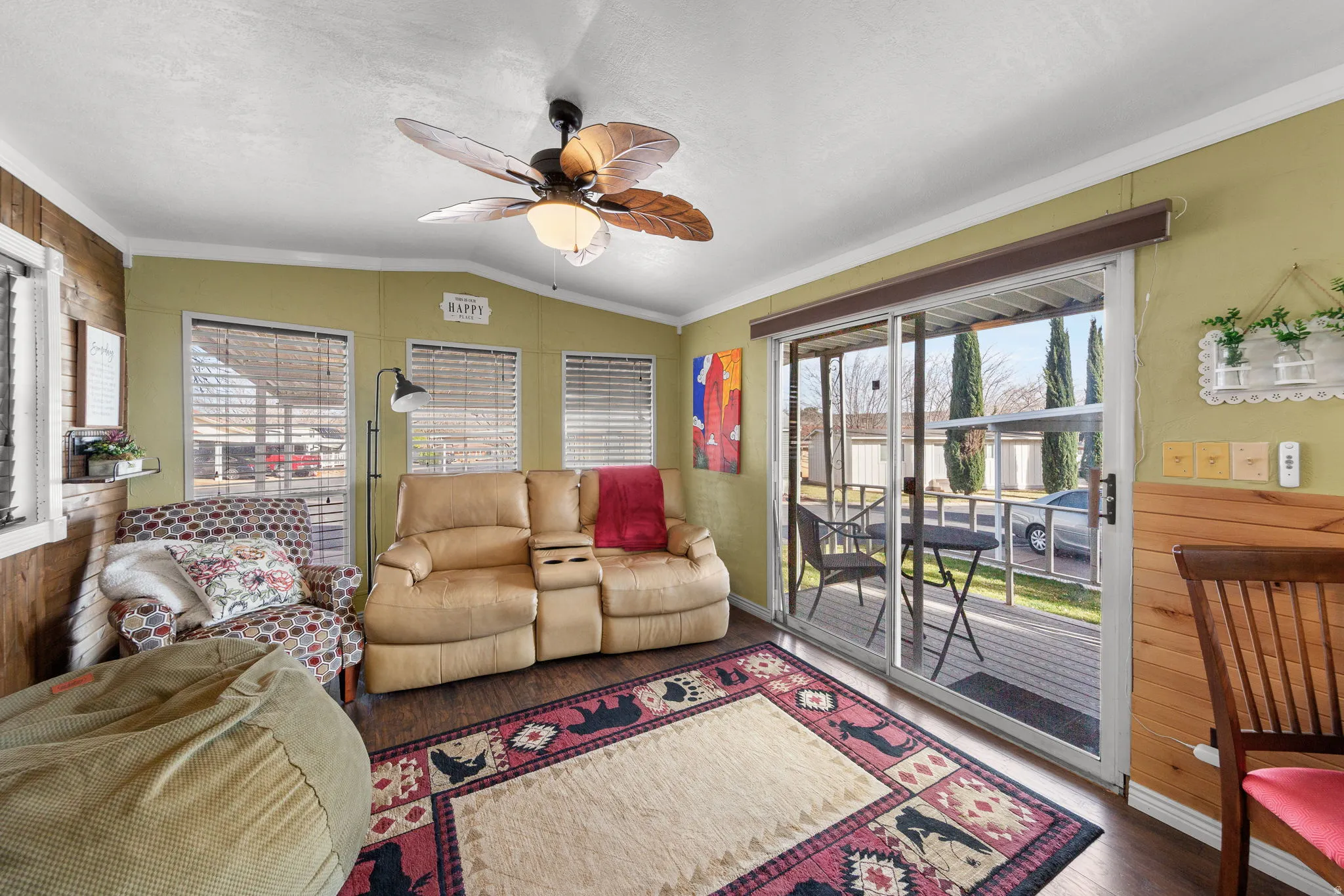 Living area featuring a ceiling fan, wooden walls, vaulted ceiling, crown molding, and wood finished floors