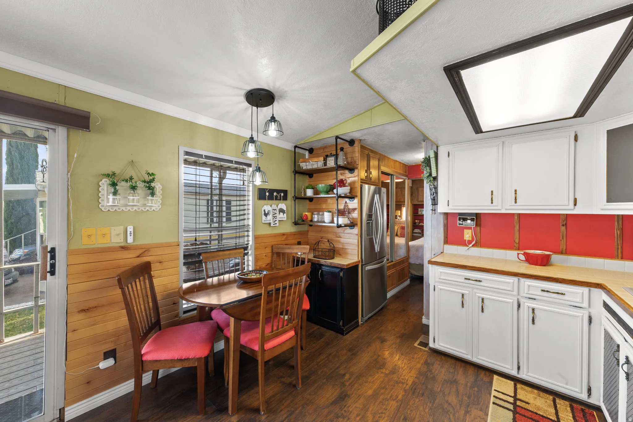 Kitchen featuring white cabinetry, dark wood-type flooring, stainless steel fridge with ice dispenser, wainscoting, and hanging light fixtures