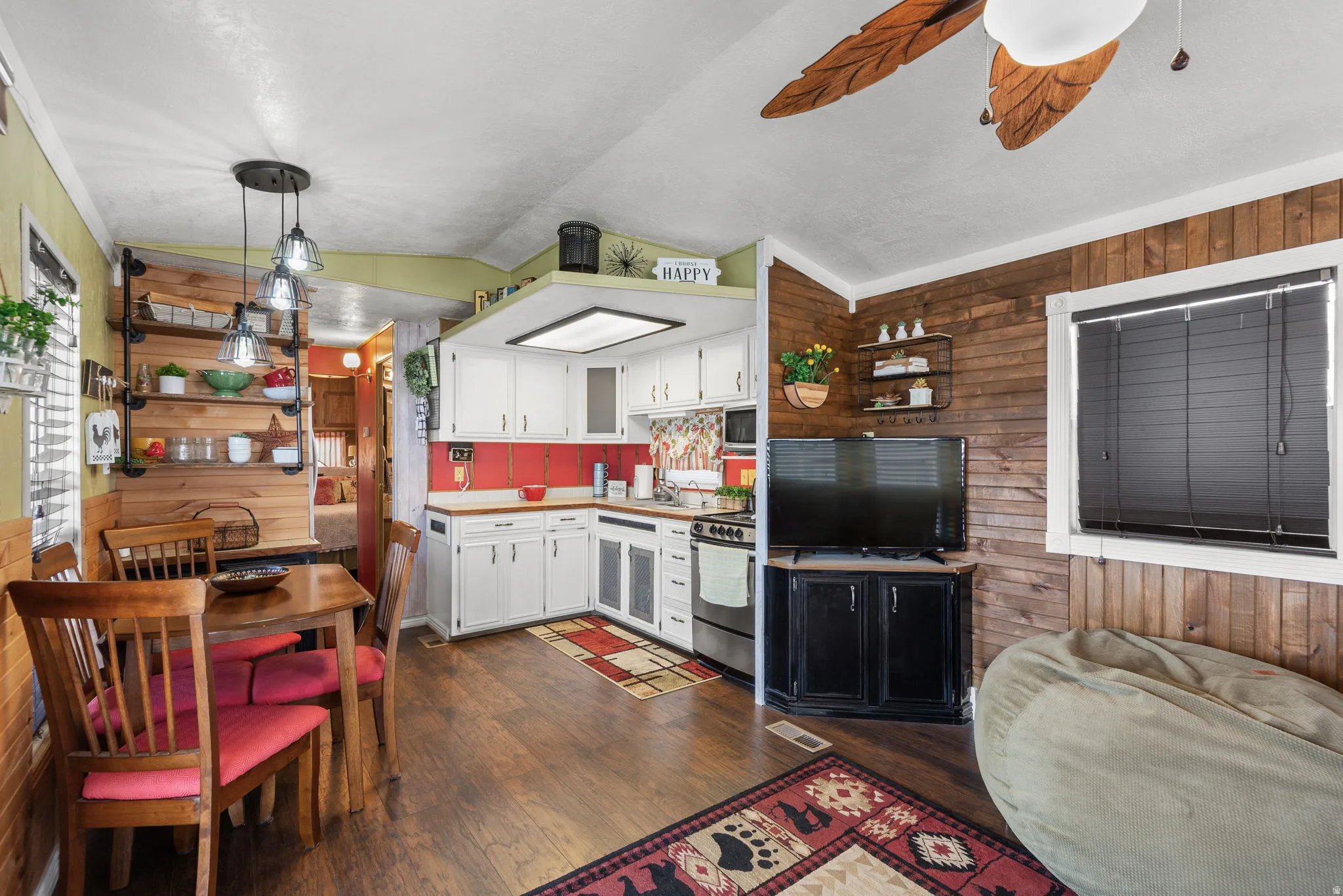 Kitchen featuring wood walls, white cabinetry, hanging light fixtures, dark wood-style floors, and lofted ceiling