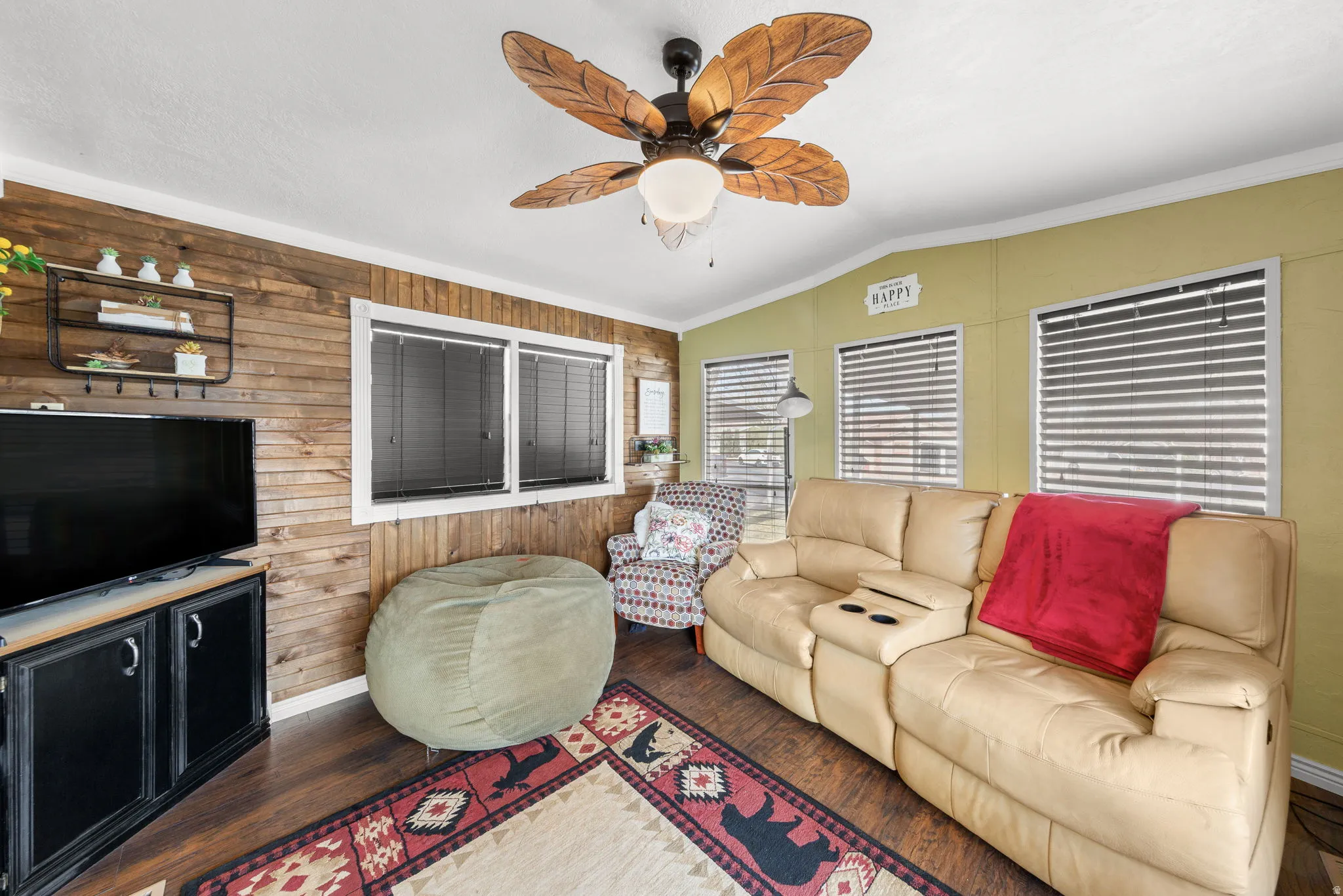 Living room featuring a ceiling fan, vaulted ceiling, wooden walls, wood finished floors, and crown molding