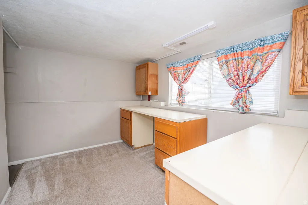 Kitchen featuring light colored carpet, light countertops, and wood finish cabinetry