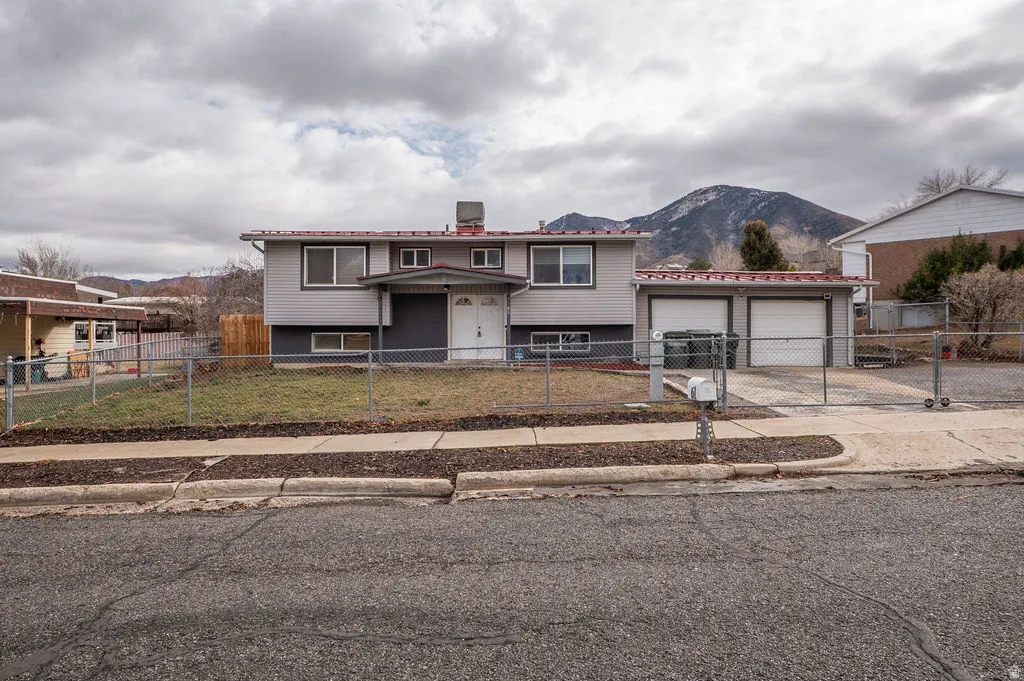 Raised ranch featuring a mountain view, a garage, a fenced front yard, a chimney, and driveway