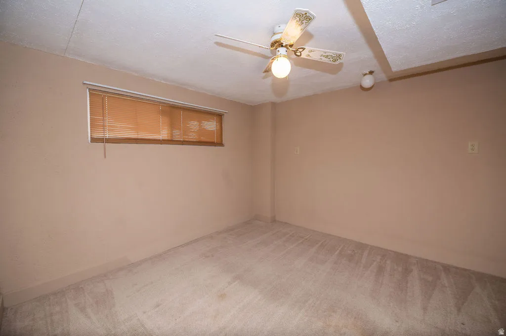 Carpeted empty room with ceiling fan and a textured ceiling