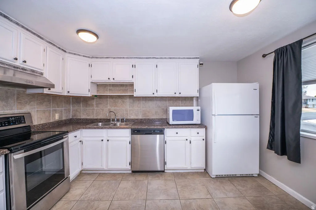 Kitchen with stainless steel appliances, dark countertops, white cabinets, backsplash, and light tile patterned floors