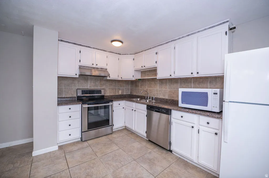 Kitchen with stainless steel appliances, white cabinets, decorative backsplash, and light tile patterned floors