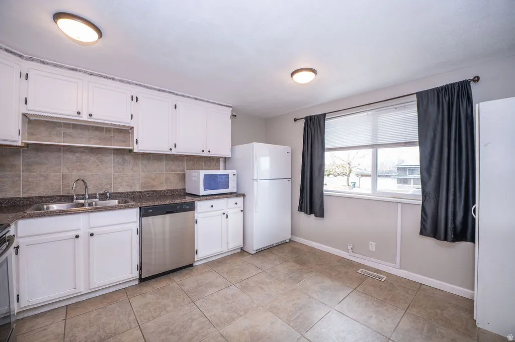 Kitchen featuring white cabinetry, stainless steel appliances, decorative backsplash, and light tile patterned floors
