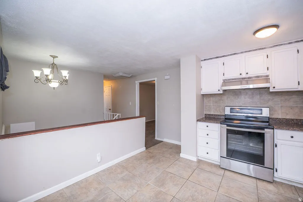 Kitchen with stainless steel range with electric cooktop, white cabinets, decorative backsplash, hanging lights, and dark stone countertops