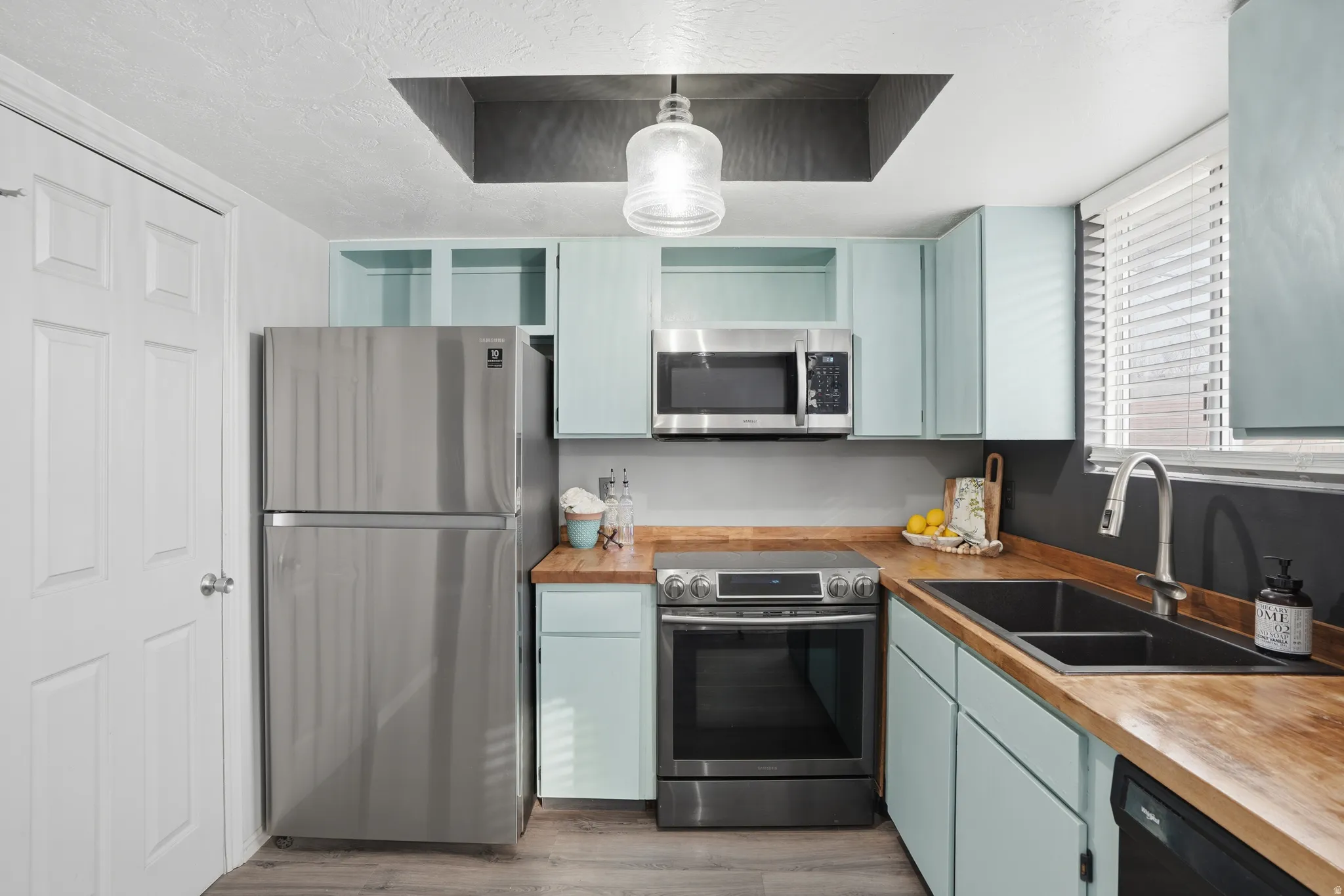 Kitchen featuring stainless steel appliances, open shelves, decorative light fixtures, blue cabinetry, and light wood-style flooring