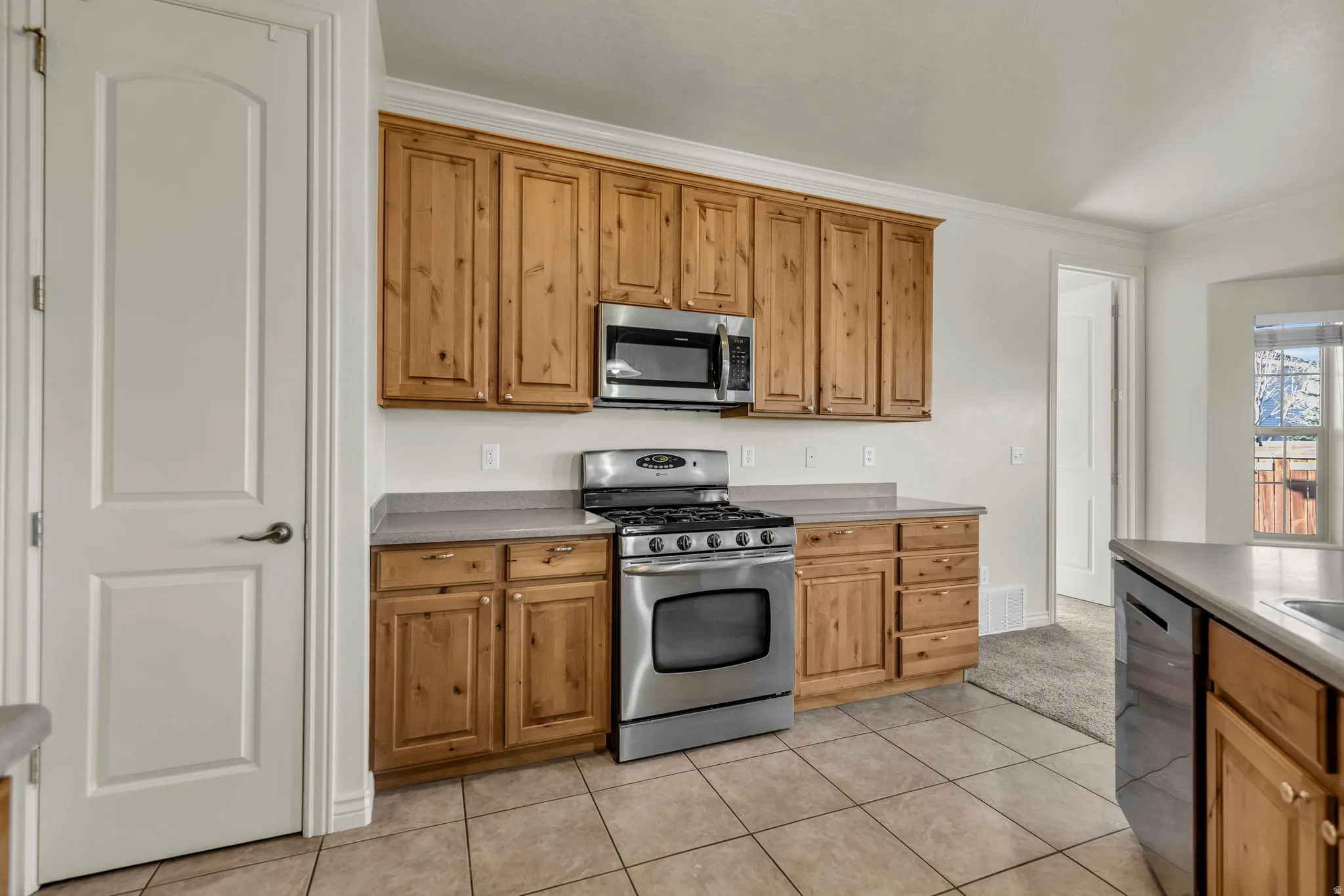 Kitchen featuring stainless steel appliances, crown molding, light tile patterned floors, wood finish cabinets, and light countertops