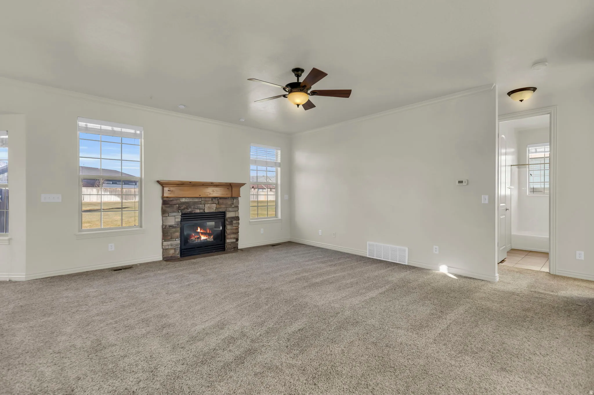 Unfurnished living room featuring ceiling fan, carpet flooring, a fireplace, and crown molding