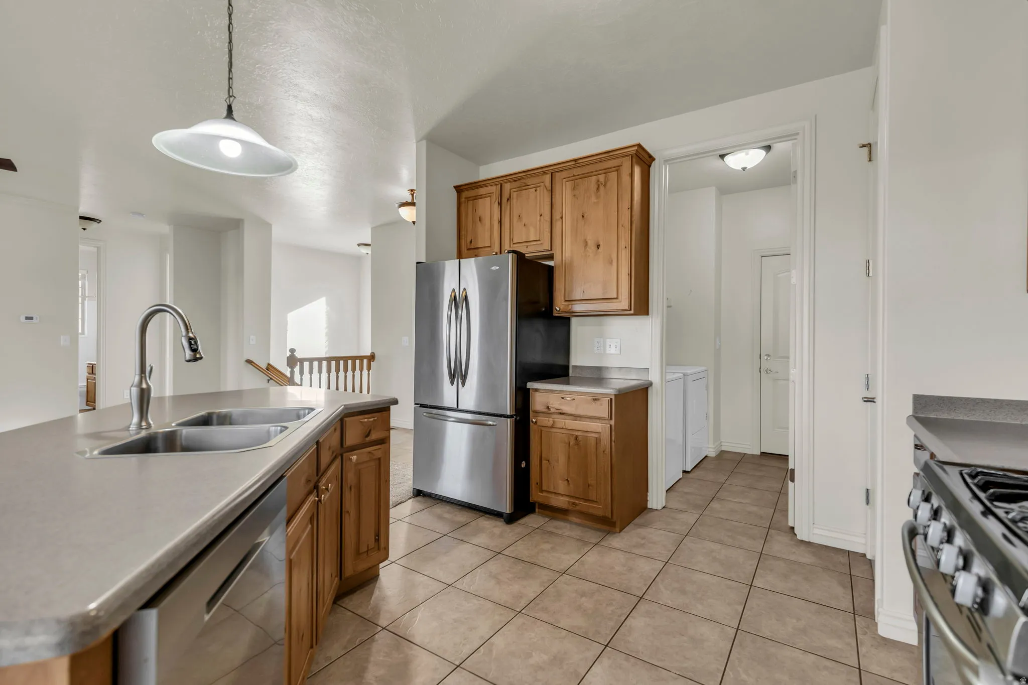 Kitchen with stainless steel appliances, an island with sink, wood finish cabinetry, decorative light fixtures, and light tile patterned flooring
