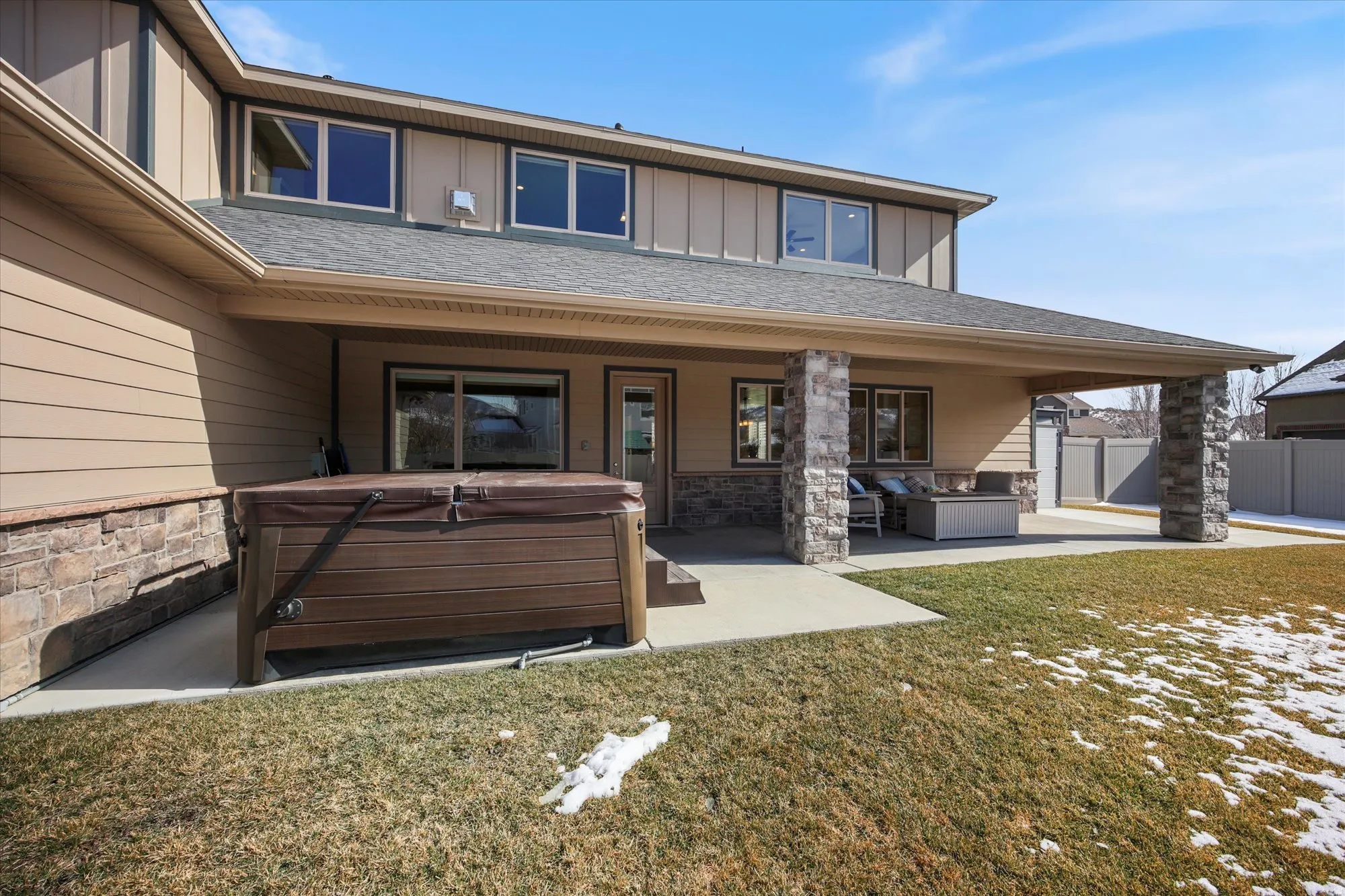 Rear view of property featuring a hot tub, stone siding, a patio, board and batten siding, and outdoor furniture