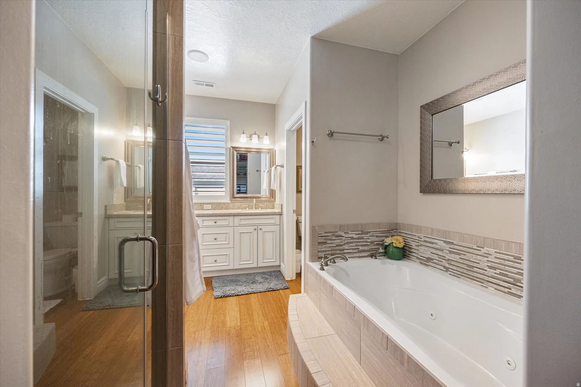 Bathroom featuring vanity, a tub with jets, light wood-style flooring, a shower stall, and a textured ceiling