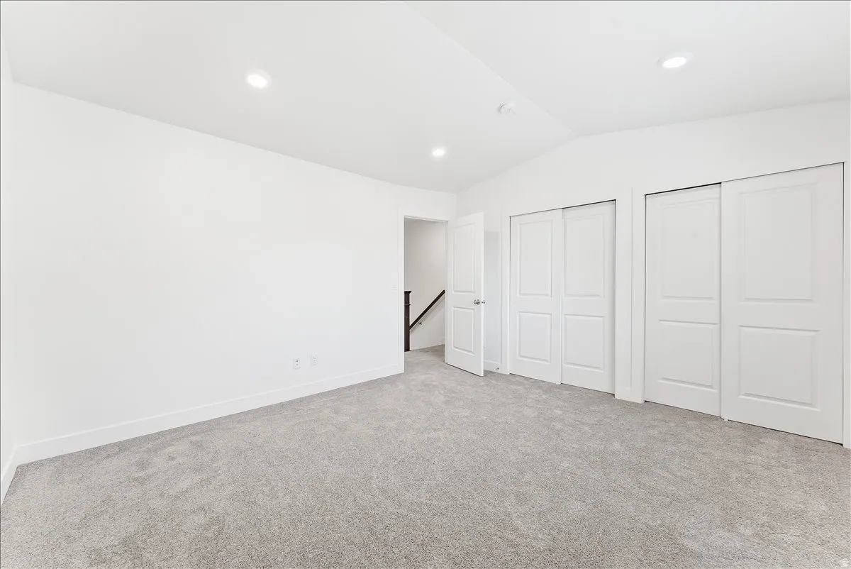 Unfurnished bedroom with lofted ceiling, multiple closets, light colored carpet, and recessed lighting
