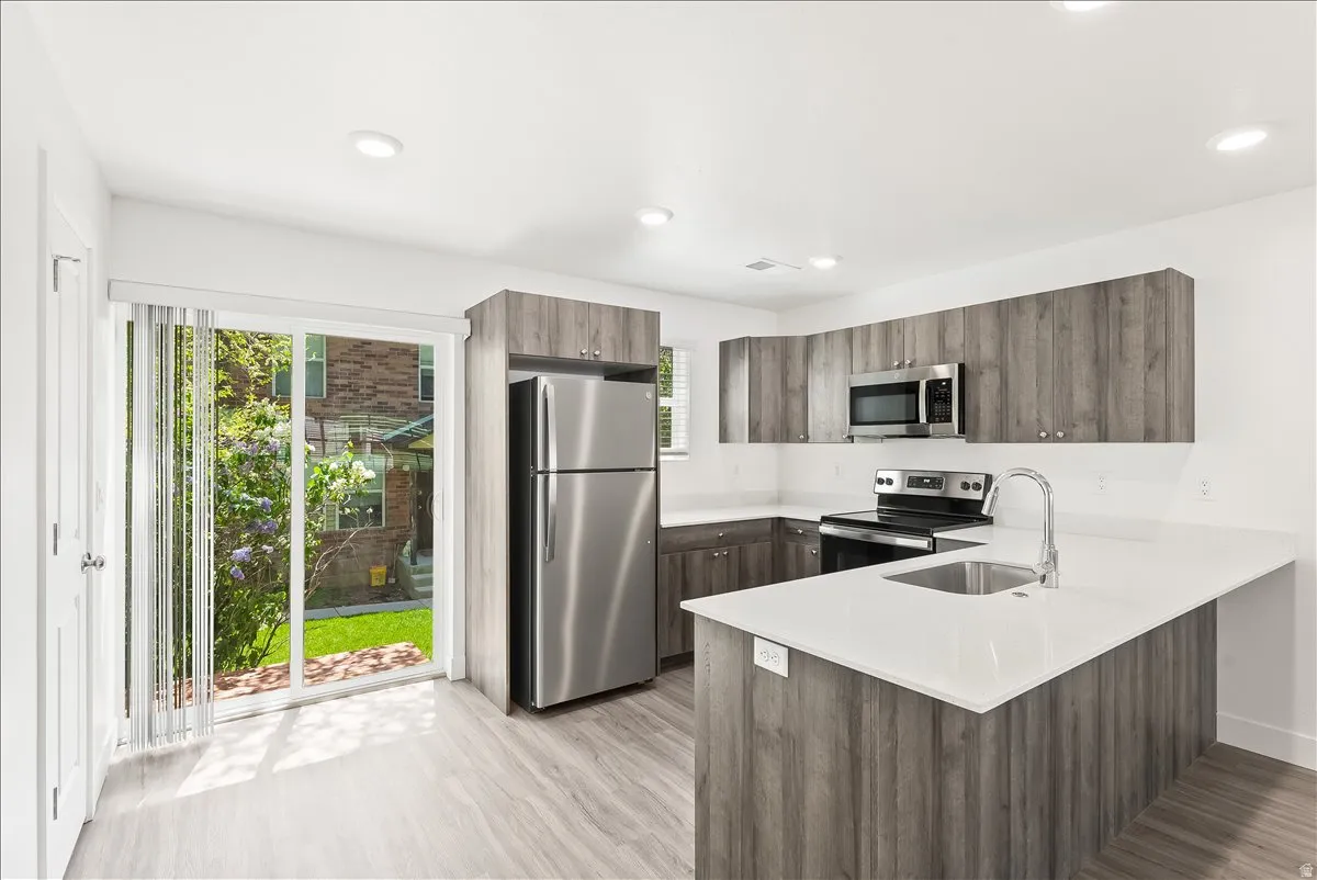 Kitchen with stainless steel appliances, a peninsula, modern cabinets, light stone countertops, and light wood-type flooring