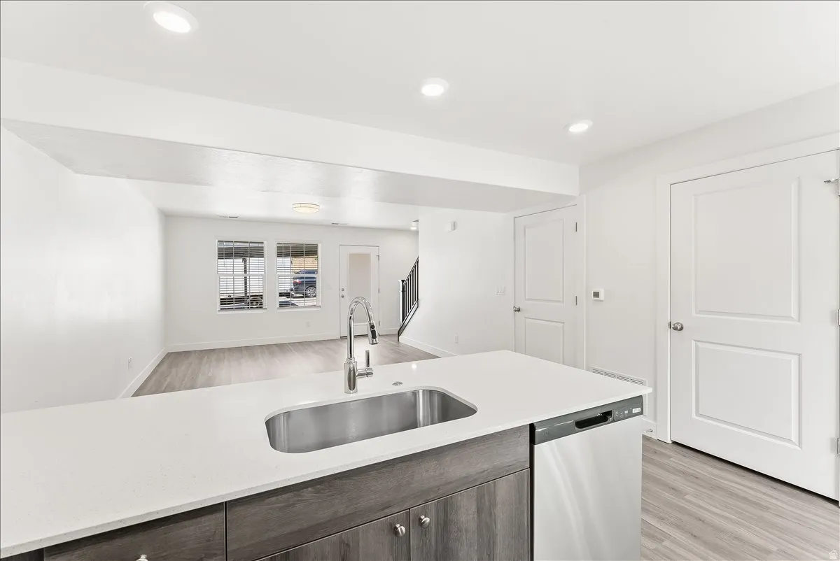 Kitchen with open floor plan, light wood-type flooring, dishwasher, light stone countertops, and recessed lighting