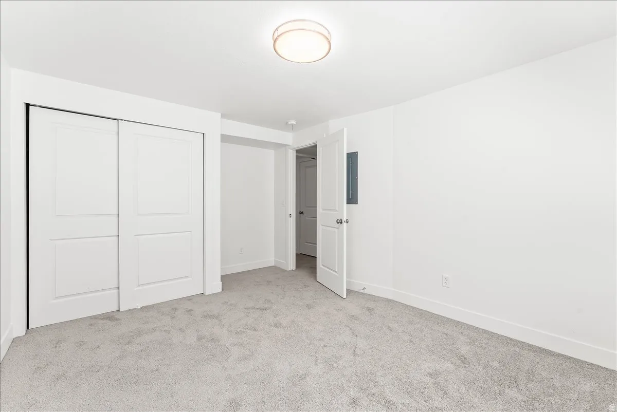 Unfurnished bedroom with light carpet, a closet, and electric panel