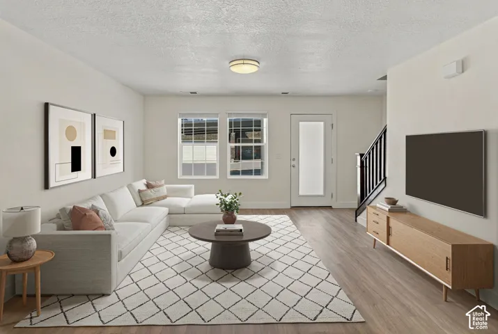 Wood-finish flooring throughout, multiple windows, a ceiling-mounted light fixture, and a stairway with a dark railing