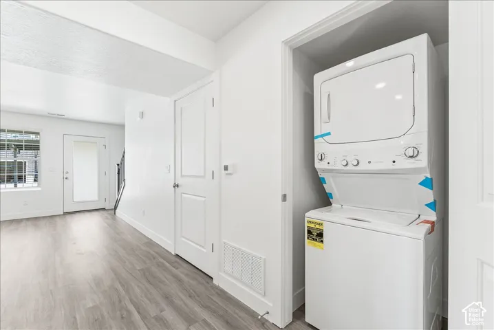 Laundry area featuring stacked washer / drying machine and light wood-style floors
