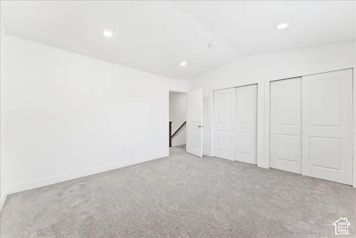 Unfurnished bedroom with lofted ceiling, multiple closets, light colored carpet, and recessed lighting