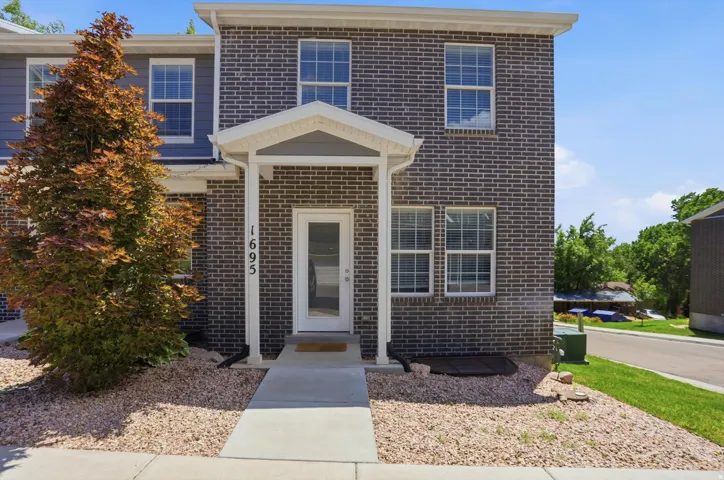 Front exterior featuring dark brick siding, white-framed windows with blinds, a covered entryway with white pillars, and a concrete walkway